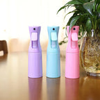 Trois vaporisateurs brumisateurs 200ml pour terrarium, coloris violet, bleu et rose, posés sur une table à côté d'une plante