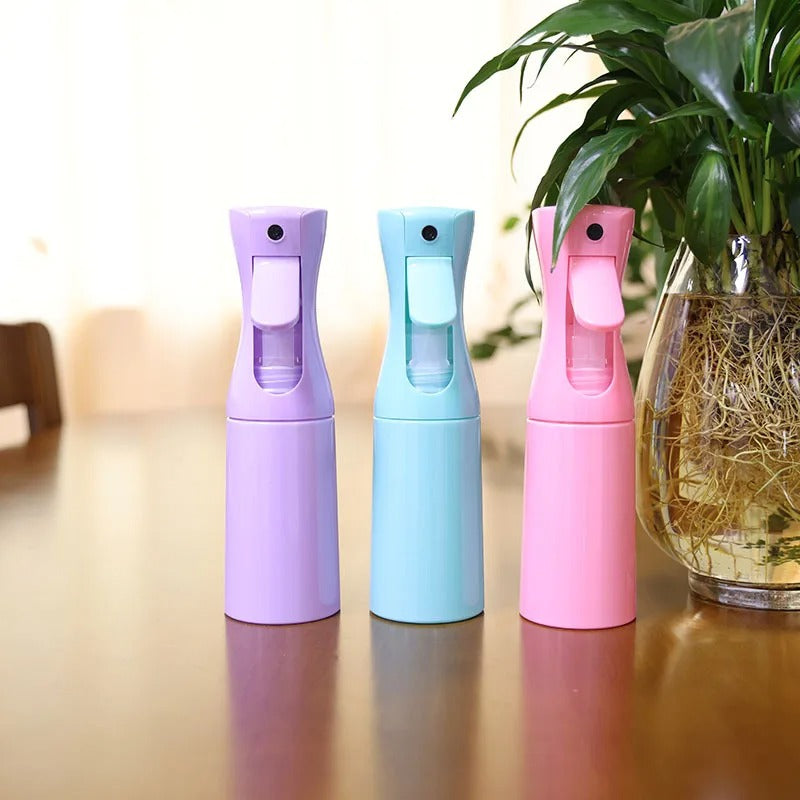 Trois vaporisateurs brumisateurs 200ml pour terrarium, coloris violet, bleu et rose, posés sur une table à côté d'une plante